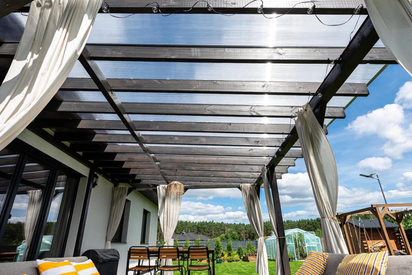 Dřevěná pergola na terase se zastřešením, závěsy a jídelním sezením